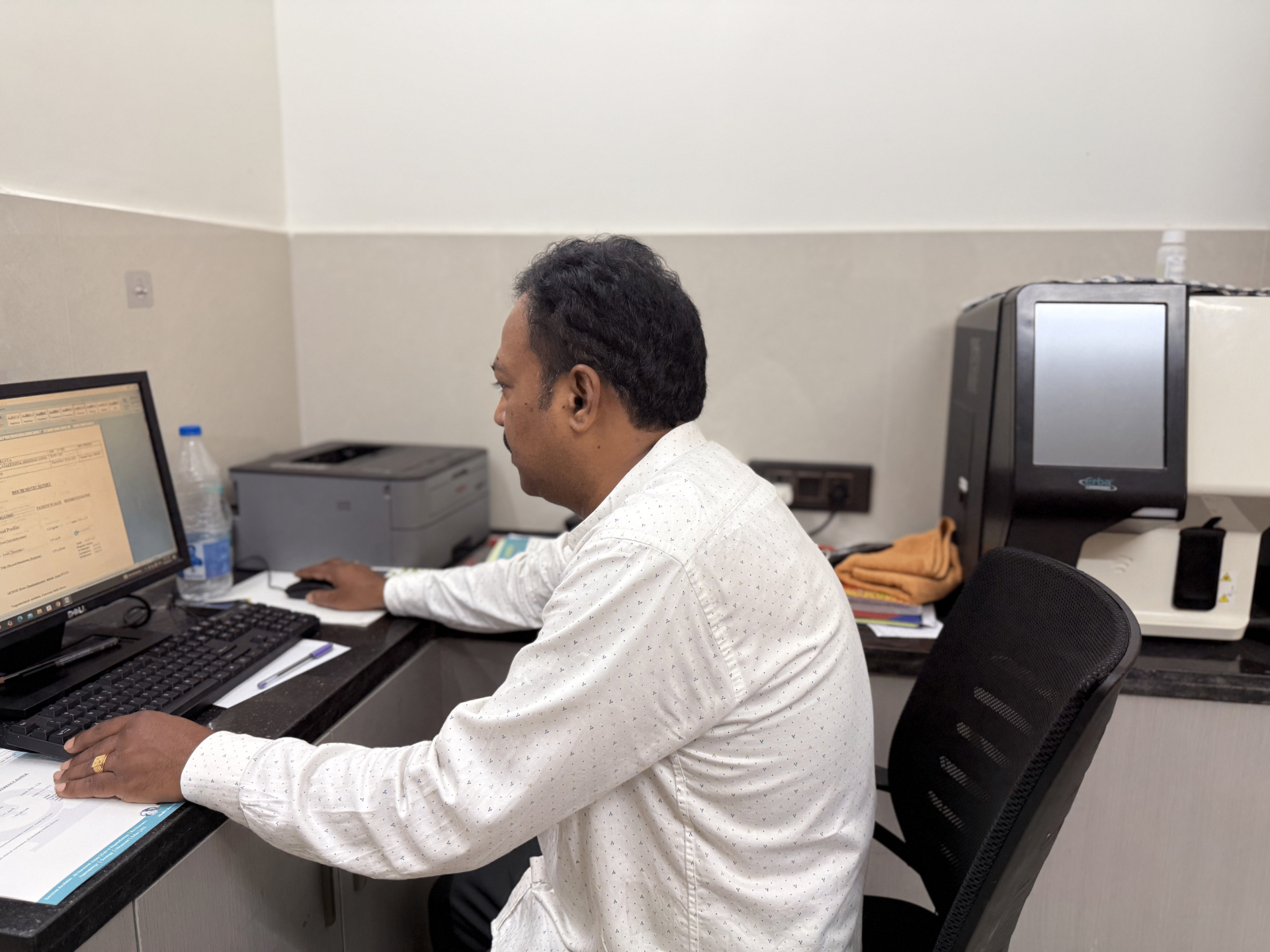 A hospital staff member working at the computer in a clinical office at Sanjeevi Hospital.