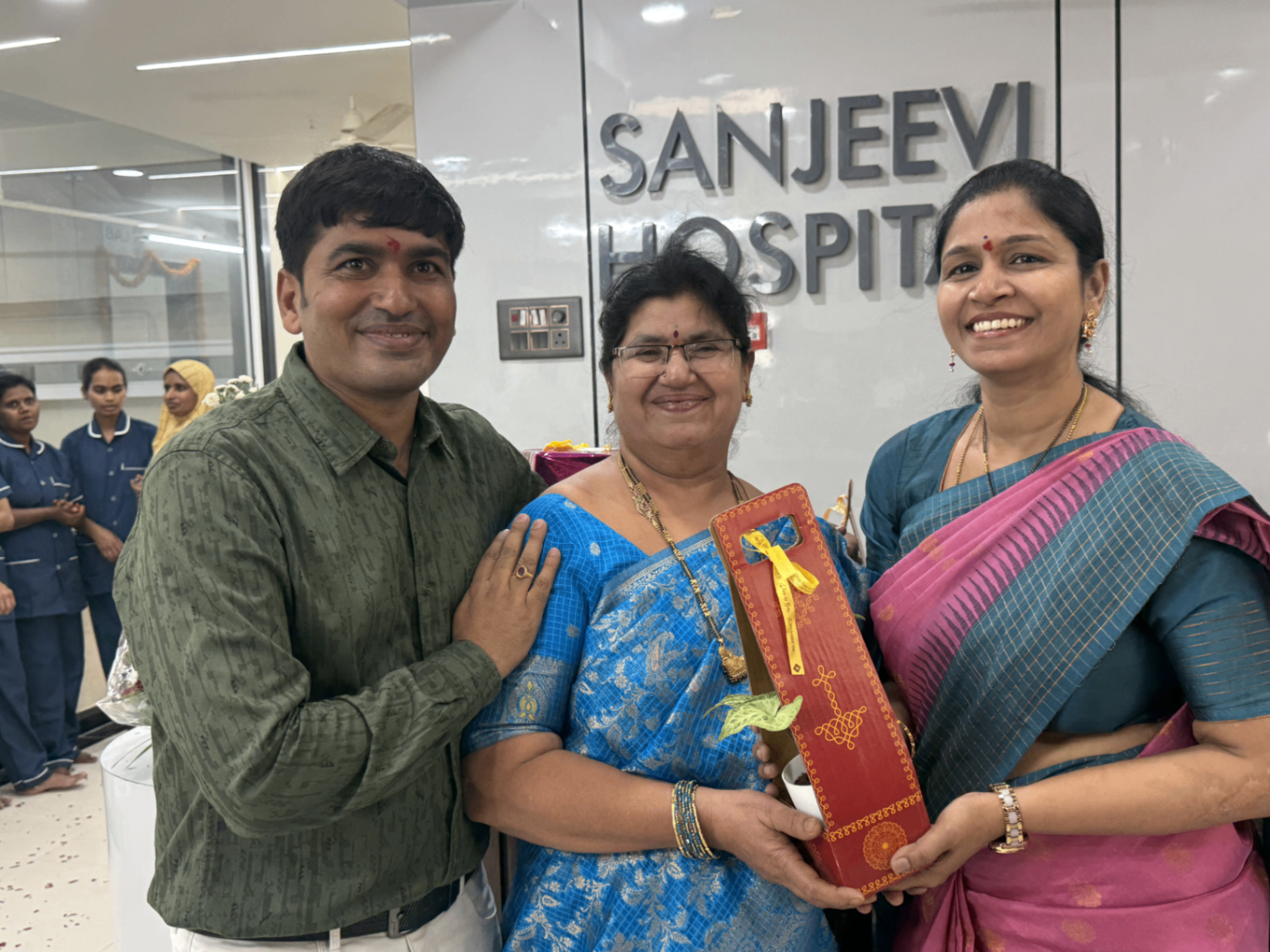 A presentation moment with hospital leadership in front of the Sanjeevi Hospital wall.